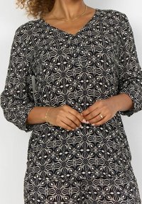 Sort og creme mønstret bluse med V-hals, lange ærmer og en løs pasform, der har et blomstermotiv gennem hele blusen.