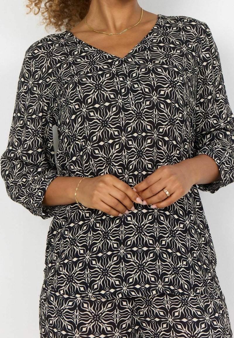 Sort og creme mønstret bluse med V-hals, lange ærmer og en løs pasform, der har et blomstermotiv gennem hele blusen.