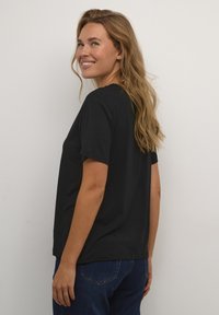 Camisa negra de algodón suave, con un corte relajado, mangas cortas y cuello redondo, combinada con unos vaqueros de mezclilla azul.