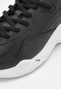 Černé kožené tenisky s texturovaným povrchem, černými tkaničkami a bílou gumovou podrážkou s decentním logem na patě.