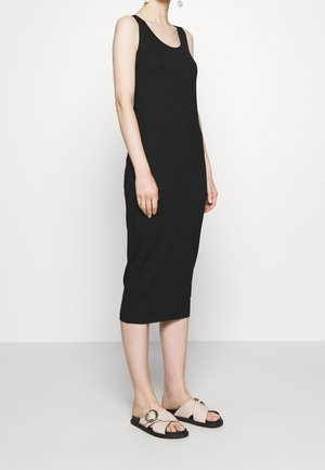 Abito midi nero senza maniche con una silhouette aderente. Abbinato a sandali slide neri e crema con un accento circolare.
