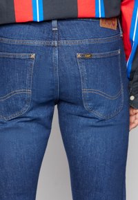 Ciemnoniebieskie dżinsy o wąskim kroju, z tylnymi kieszeniami z zakrzywionymi szwami oraz delikatną, skórzaną metką z logo na pasku.