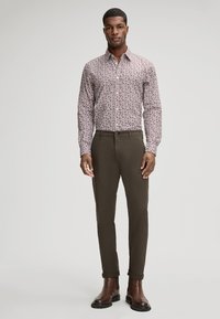 Lange mouwen, knoopsluiting shirt met een klein bloemenpatroon in tinten van roze, gecombineerd met op maat gemaakte donkergroene chino's en bruine enkellaarsjes.