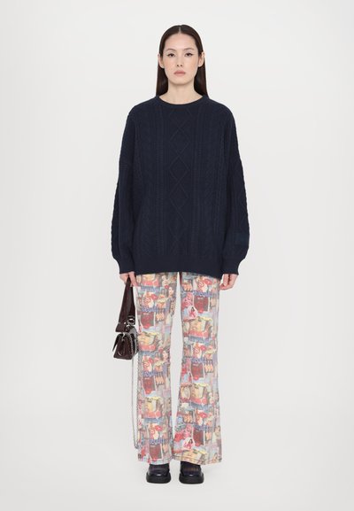 Pull en maille bleu marine avec un motif torsadé, associé à un pantalon large à imprimé collage coloré. Accessoirisé avec un petit sac à main foncé.
