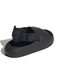 Svart slip-on sandal med rund tå, tillverkad av gummiliknande material. Har en justerbar rem och präglad logotypdetalj på sidan.