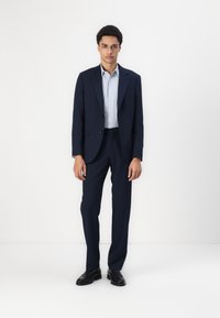 Marineblaues Anzug mit einreihigem Sakko, hellblauem Hemd und maßgeschneiderten Hosen. Getragen mit schwarzen Leder-Lederschuhen. Glatte Stoffstruktur.