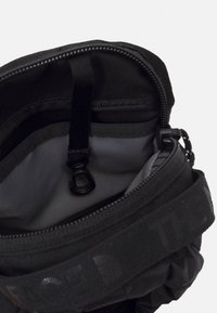 Borsa in tessuto nero con apertura con zip, dotata di interno grigio, tracolla regolabile e clip interna per fissare gli oggetti.