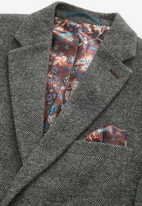 Grau karierter Blazer mit einem bunten, floral gemusterten Innenfutter, ausgestattet mit einem Einstecktuch in passenden Farben und Texturen.