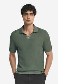 Grön kortärmad polo shirt tillverkad av strukturerad stickad tyg, med en krage och V-hals samt subtila randdetaljer.