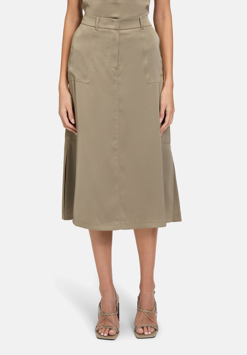 Jupe midi kaki avec une taille ajustée, poches avant et fentes sur les côtés. Fabriquée en tissu lisse avec un léger éclat. Sandales à lanières visibles.
