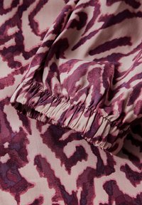 Paars en roze gestippeld stof met een gathered elastische manchet, dat een gladde textuur en abstract design toont.