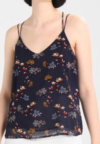 Woman wearing a navy floral sleeveless top with thin shoulder straps and a V-neck.