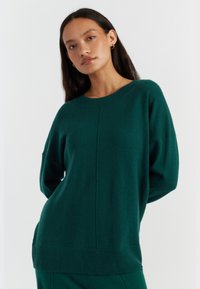 Pull en maille vert émeraude avec un col rond, une coupe décontractée, des épaules tombantes et un ourlet droit côtelé. Texture douce et finitions minimales.