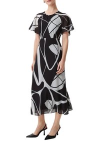 Czarna i biała sukienka w deseń z krótkimi falbaniastymi rękawami, okrągłym dekoltem i swobodną sylwetką. W połączeniu z czarnymi sandałami na obcasie.