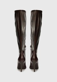 Botas marrones de cuero por encima de la rodilla con acabado brillante, tacones de aguja altos, cremalleras traseras y un diseño ajustado.