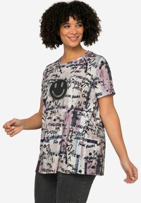 T-shirt à manches courtes et col rond dans des couleurs pastel, avec un graphique de smiley noir et des motifs de texte manuscrit, fabriqué en tissu doux et léger.