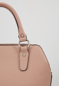 Sac à main en cuir rose doux avec poignée arrondie fixée par un anneau en argent et détails de couture sur un fond clair uni.