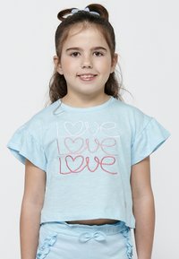 Gaiši zils īsais krekls ar plīvurojošām piedurknēm, kas rotāts ar krāsainu izšuvumu "love" rozā, sarkanā un baltā krāsā. Gluda auduma struktūra.