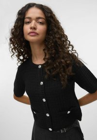 Zwarte cropped cardigan in een gestructureerde gebreide stof, korte mouwen, met vijf glanzende knopen aan de voorkant en twee kleine zakken.