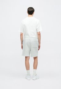 Szürke rövidnadrág elasztikus derékrésszel és egy hátsó zsebbel, fehér rövid ujjú pólóval párosítva. A modell hátulról látható.