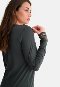 Haut gris à manches longues avec une coupe ajustée. Accent en dentelle transparente sur les poignets et texture lisse. Le col est arrondi.