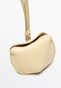 Borsa a sacchetto in pelle beige con una forma curva, dotata di manico annodato e dettaglio di cuciture visibili lungo i bordi.