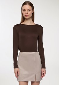 Brązowa bluzka z długim rękawem i dekoltem w łódkę, zestawiona z jasnobeżową mini spódnicą z przodem rozciętym i miękką, gładką fakturą.