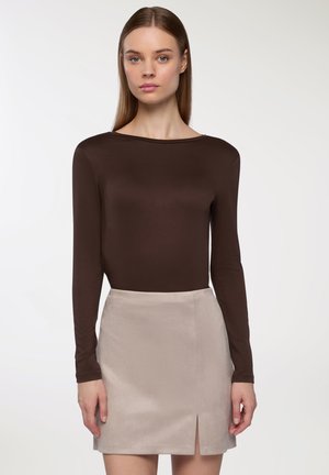Maglietta marrone a maniche lunghe con scollo a barca, abbinata a una mini gonna beige chiaro con uno spacco frontale e una texture morbida e liscia.