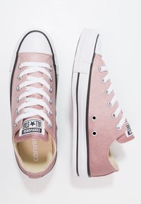 Růžové třpytivé tenisky Converse All Star s bílými tkaničkami, gumovou špičkou a černým akcentovým pruhem na podrážce. Logo na jazyku.