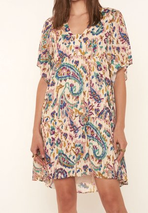 Woman wearing a loose, short-sleeve dress with a multicolored abstract paisley pattern in shades of blue, purple, green, and gold.
