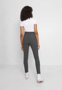 Black and white checkered trousers with a high waist and slim fit, featuring back pockets, paired with a fitted white t-shirt and white sneakers.