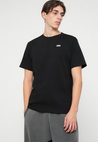 T-shirt de algodão preto com decote redondo e mangas curtas, apresentando um pequeno logótipo branco no peito. Textura suave e ajuste descontraído.