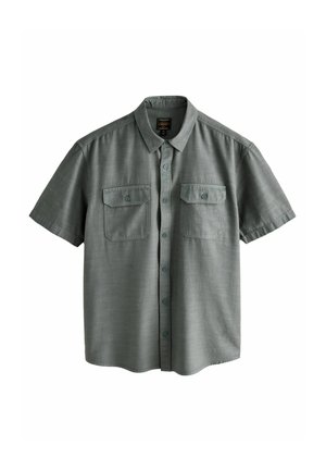 Camisa de botones de manga corta en verde apagado. Presenta dos bolsillos en el pecho, un cuello puntiagudo y una tela suave y texturada.