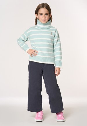 Maglione dolcevita turchese chiaro con righe bianche, polsini a coste, abbinato a pantaloni ampi blu navy e sneakers rosa.