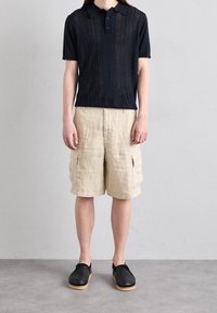 Námořnická polo tričko s krátkým rukávem a texturovaným designem; béžové cargo šortky dosahující ke kolenům s kapsami; černé kl slip-on boty se dřevěnými podrážkami.