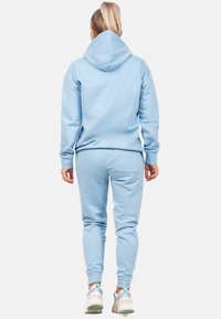 Hoodie azzurro chiaro e joggers abbinati realizzati in tessuto morbido; presenta un grande cappuccio, maniche a polsino e bande elastiche alle caviglie.