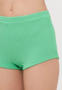 Boyshort verde a coste con elastico in vita, caratterizzati da una texture liscia e un design aderente, tagliati a metà coscia.