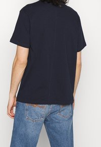 Mörkblå bomullströja med korta ärmar och rak skärning, bärs med ljusblå denimjeans med kontrasterande sömmar och fickdetaljer.