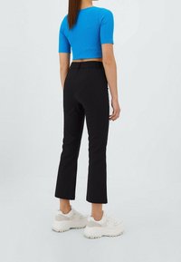 Crop top bleu à rayures avec des manches courtes, associé à un pantalon noir ajusté. Des baskets blanches complètent la tenue. Design simple et moderne.