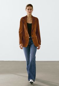 Brun läderblazer med skräddarsydd passform, enfärgad design, två knappar och slagkrage, i kombination med ljusblå utsvängda jeans.