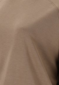 Brun, slät tyg med en lätt lyster, med avslappnad passform och minimala söm detaljer. Texturen verkar mjuk och lätt.