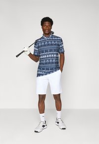 Polo shirt blu con motivo a palme, pantaloni corti bianchi e mazza da golf. Dotato di colletto, maniche corte e scarpe sportive.