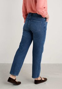 Donkerblauwe denim jeans met een recht gesneden pijp, voorzien van twee achterzakken en een tailleband. Gemaakt met bruine suède Mary Jane-schoenen.