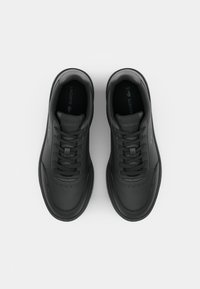 Črne usnjene superge z gladko površino, okroglo konico, oblazinjenim ovratnikom in ravnimi vezalkami. Diskretna logo podrobnost na strani in jeziku.