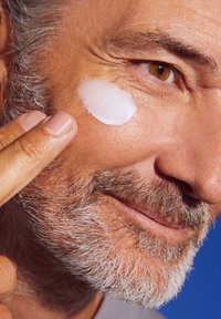 Moisturizing cream applied to facial skin; visible light cream texture; tan skin with facial hair; blue background.