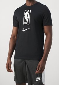 Camiseta de algodón negra con el logo blanco de la NBA y el swoosh de Nike. Manga corta, cuello redondo, corte relajado, textura suave.