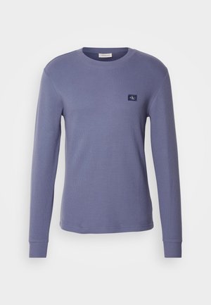 Langärmliges Rundhals-Shirt aus leichtem lila Baumwollstoff mit gerippter Textur und kleinem Logopatch auf der Brust. Flacher Saum und eng anliegende Bündchen.