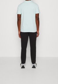 Camiseta de manga corta azul claro, joggers negros y zapatillas grises con acentos triangulares distintivos en la suela. Diseño simple, corte relajado.