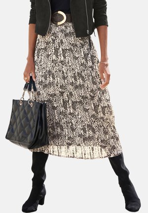 Woman wearing black jacket, animal print pleated skirt, black heeled boots, holding black quilted handbag by side.