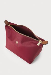 Burgunder nylonpouch med gullglidelås, lærdetaljer og logo. Åpnes fra toppen, myk tekstur, kompakt design egnet for ulike bruksområder.